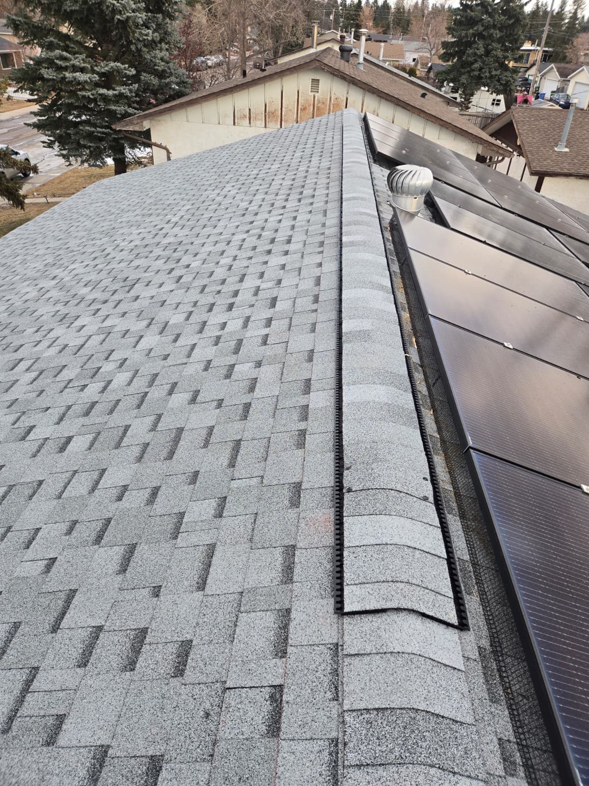 Ridge vent beside solar panels on a grey shingle roof